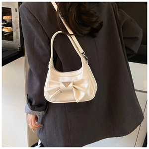 Detail of cream white half-moon bag featuring a large bow and triangular metal logo