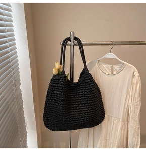 Detail of black woven straw tote bag texture with long straps in a lifestyle setting