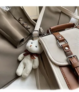 Detail of cream and brown shoulder bag with plush bear charm and metallic buckle