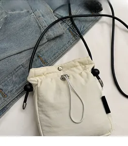 Detail of cream drawstring crossbody phone bag with black cord strap on denim background