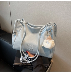 Detail of light blue leather tote bag with embossed logo and white plush charm on books