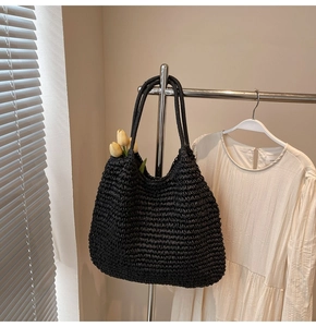 Détail d'un grand sac cabas en paille noire avec texture tissée délicate sur un support métal