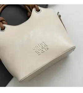 Détail d'un sac seau en cuir crème avec poignée tressée marron et œillets en métal