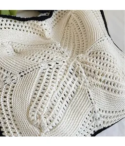 Detailed close-up of hollowed crochet knit pattern in cream with black contrast edges