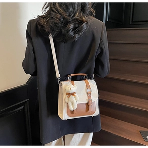 Close-up of retro two-tone crossbody bag with white plush bear charm and buckle straps