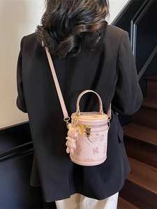 Pink cylinder bucket bag with bear embossing and charms worn by model as a crossbody