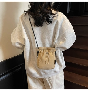 Detail of a beige drawstring crossbody bucket bag with black strap worn by a model