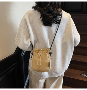 Detail of khaki drawstring crossbody bucket bag showing nylon texture and shoulder strap