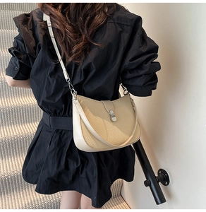 Close-up of crescent straw woven crossbody bag with cream leather trim and silver metal lock