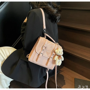 Detail of pink PU leather mini backpack with a white plush bear charm on wooden steps