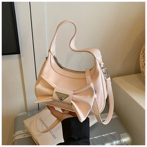 Detail of light pink shoulder bag with large bow decoration and metal logo plaque
