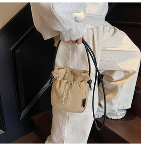 Detail of the drawstring closure and textured fabric on the beige crossbody bucket bag