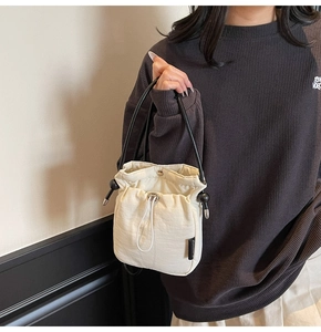 Detail of white drawstring bucket bag with black thin strap worn by a female model