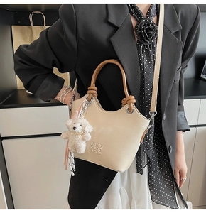 Détail du sac seau beige avec poignée marron, bandoulière et un petit pendentif ours