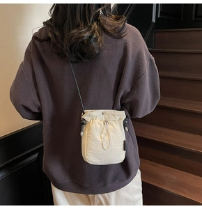 Detailed view of cream nylon drawstring crossbody bucket bag on a model on stairs