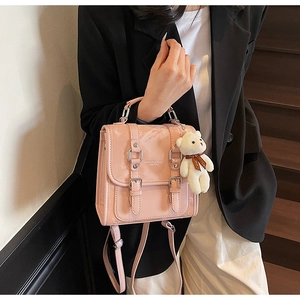 Pink glossy backpack with silver buckles and a white plush bear charm shown on a model