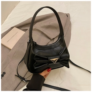 Detail of black leather handbag with decorative bow and triangular metal logo on bed
