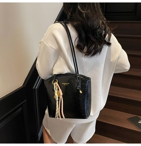 Dettaglio di una borsa tote in pelle nera lucida con logo dorato e ciondolo a nappa rosa intrecciata