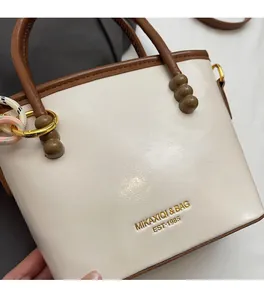 Detailed close-up of cream bucket bag with brown trim and embossed gold logo
