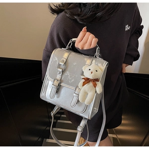 Detail of silver metallic backpack featuring metal chain handle and plush bear charm