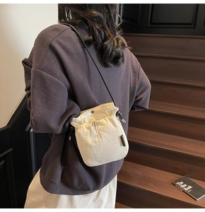 Close-up of minimalist cream drawstring bucket bag with black rope strap on model