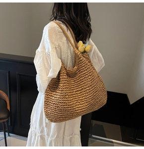 Détail d'un grand sac cabas en paille porté par un mannequin en robe blanche