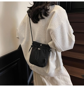 Model wearing a black drawstring bucket crossbody bag against a minimalist background