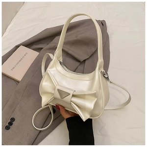 Close-up of cream bow handbag with metallic triangle accent and detachable strap