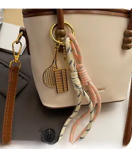 Close-up of golden keychain with mini tennis racket and abacus on contrast bucket bag