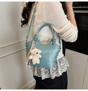 Détail d'un sac seau bleu clair avec poignée argentée et charmant ours en peluche