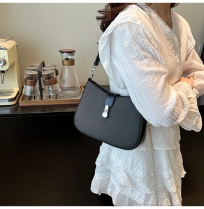 Detail of black woven crescent bag with silver buckle worn on a lace dress