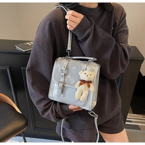 Detail of silver metallic crossbody bag featuring double buckles and a plush bear charm