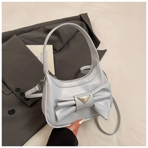 Detailed view of crescent shoulder bag featuring large bow and metallic triangle plaque
