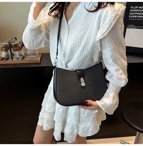 Detail of black woven half-moon crossbody bag with silver clasp on white lace dress