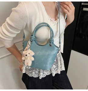 Détail du sac seau bleu avec gaufrage de lettres, pendentif ours en peluche et foulard