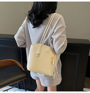 Dettaglio borsa tote color crema con logo dorato e ciondolo in corda intrecciata alla moda