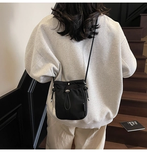 Rear view of a black drawstring mini bucket bag worn by a model on wooden stairs