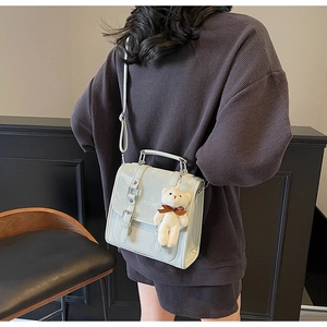 Close-up of glossy patent leather handbag with buckle details and plush bear charm