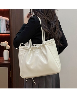 Détail du sac fourre-tout crème avec nœuds montrant la texture en cuir brillant et la bandoulière