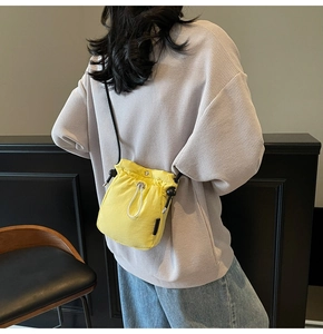 Detail of yellow nylon drawstring crossbody bag with black adjustable strap and tag