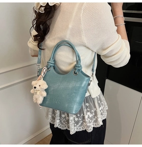 Sac seau bleu structuré avec breloque ours en peluche porté par un mannequin chic