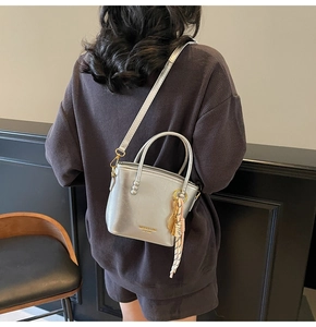 Detail view of a silver metallic bucket bag with dual handles and tennis racket charm