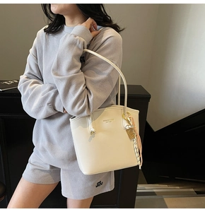 Dettaglio di una borsa tote in pelle bianco crema con finiture dorate e nappa decorativa