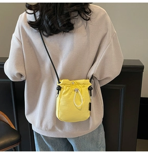 Close-up of bright yellow drawstring bucket bag with black strap on a waffle sweater