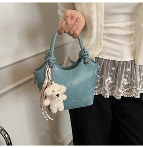Détail du sac seau bleu clair avec poignée nouée et accessoire de charme de chien en peluche