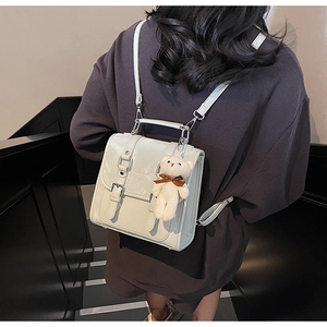 Detail of cream white leather backpack featuring metal buckles and a cute plush bear charm