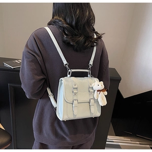 Detail view of a light green mini backpack featuring decorative buckle straps and a plush bear