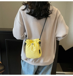 Detail of yellow drawstring crossbody bag with black strap and gray sweater outfit