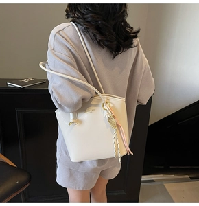 Dettaglio di una borsa tote in pelle bianca con logo dorato e nappa colorata decorativa