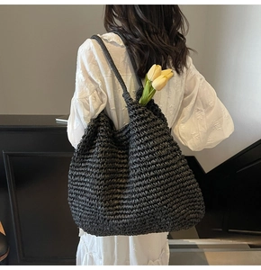 Detailed view of the woven black straw tote bag texture and reinforced handles
